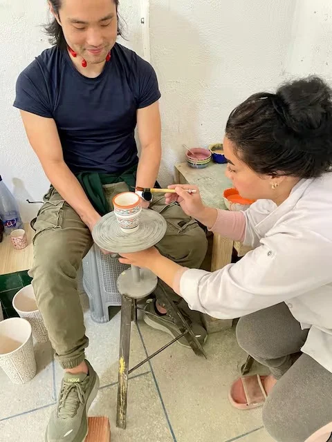 Visitor painting a cup guided by an artisan